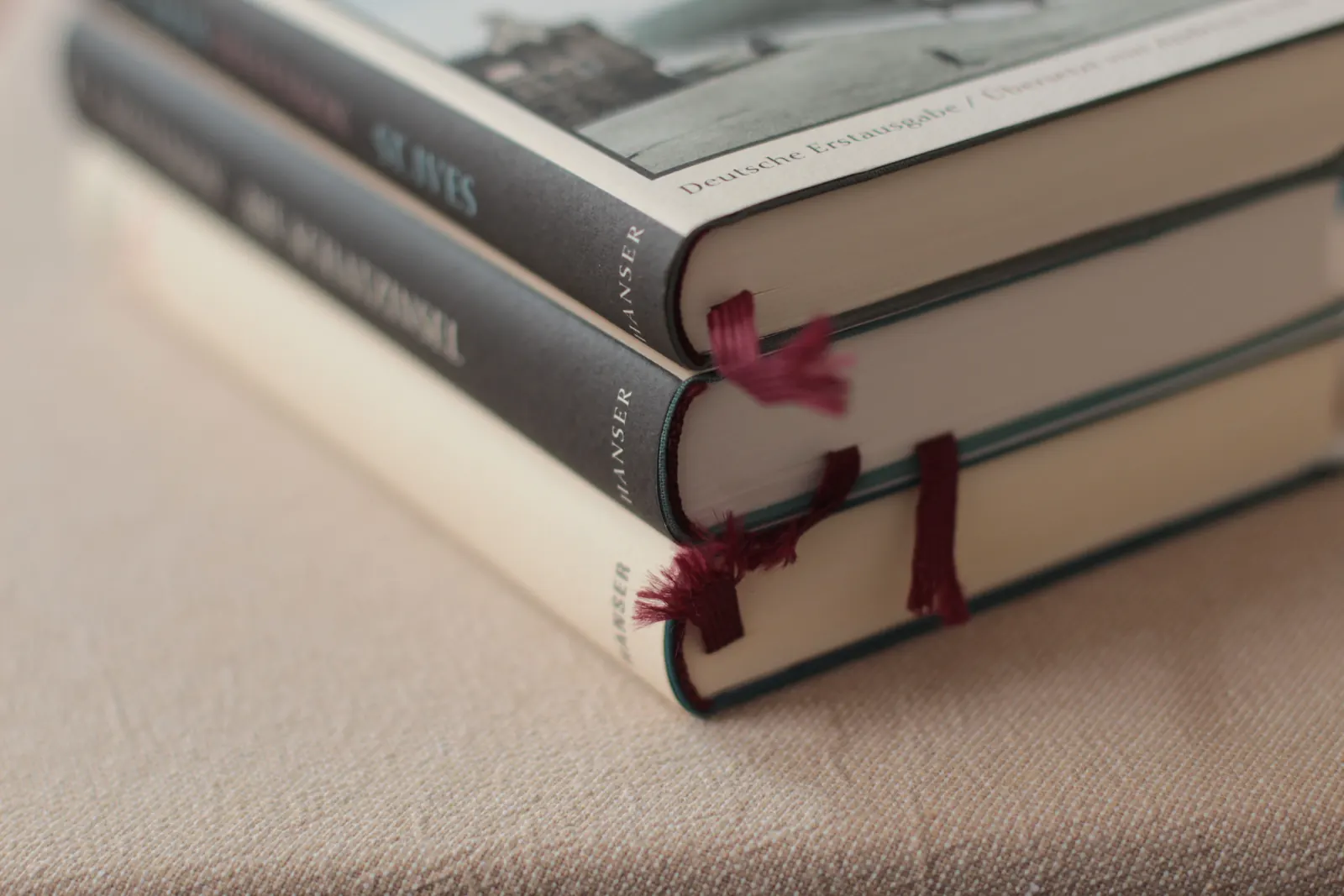 Pile de livres reliés sur une table beige chaude, avec de fins signets, en lumière du jour douce.